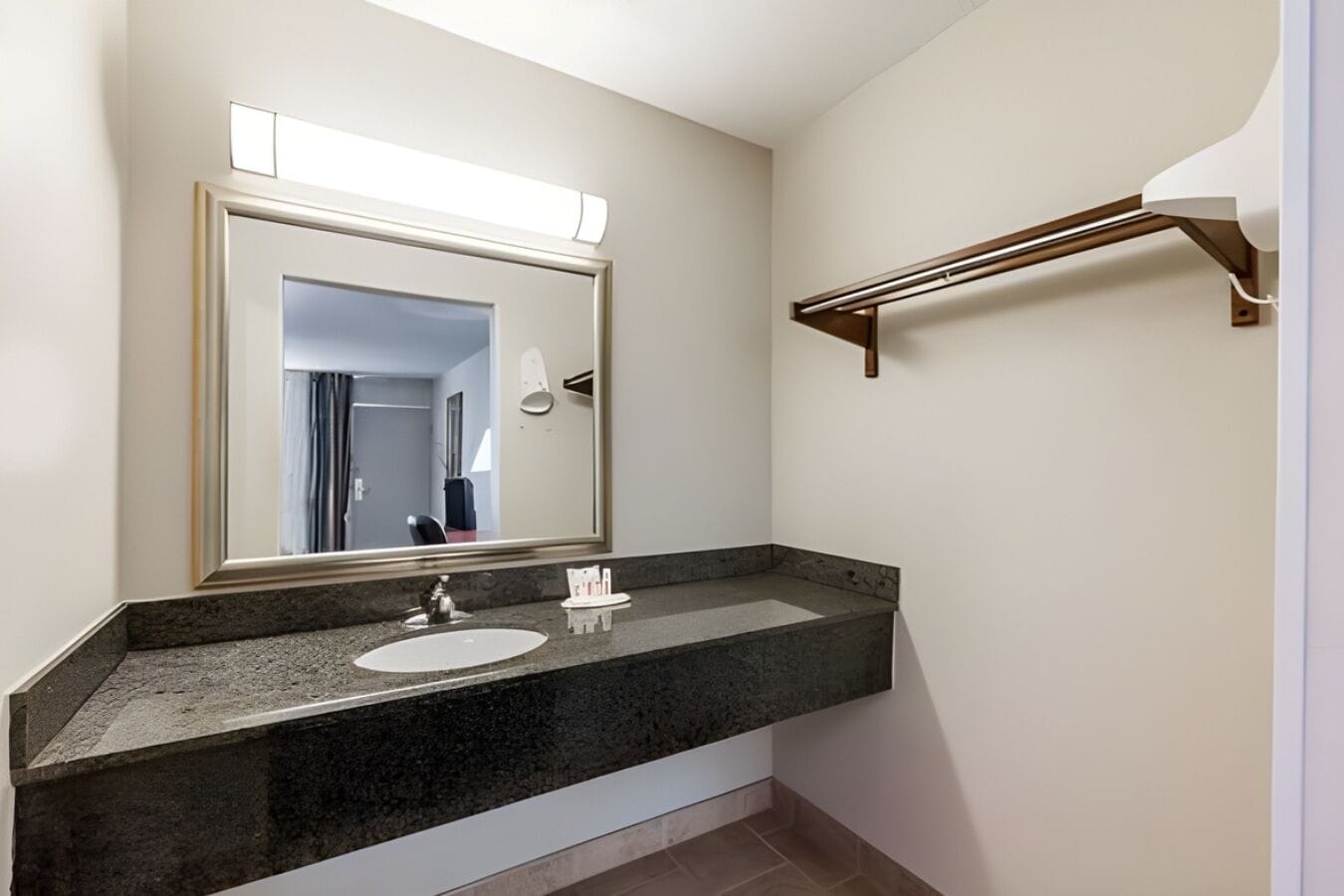 A bathroom with a granite countertop, a white sink, a large mirror, and a towel rack.