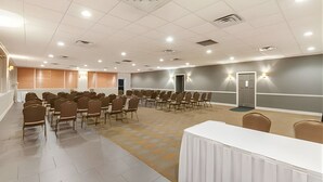 A conference room with rows of chairs, a white table, and a projector screen. - Iberia House & Suites (New Iberia)