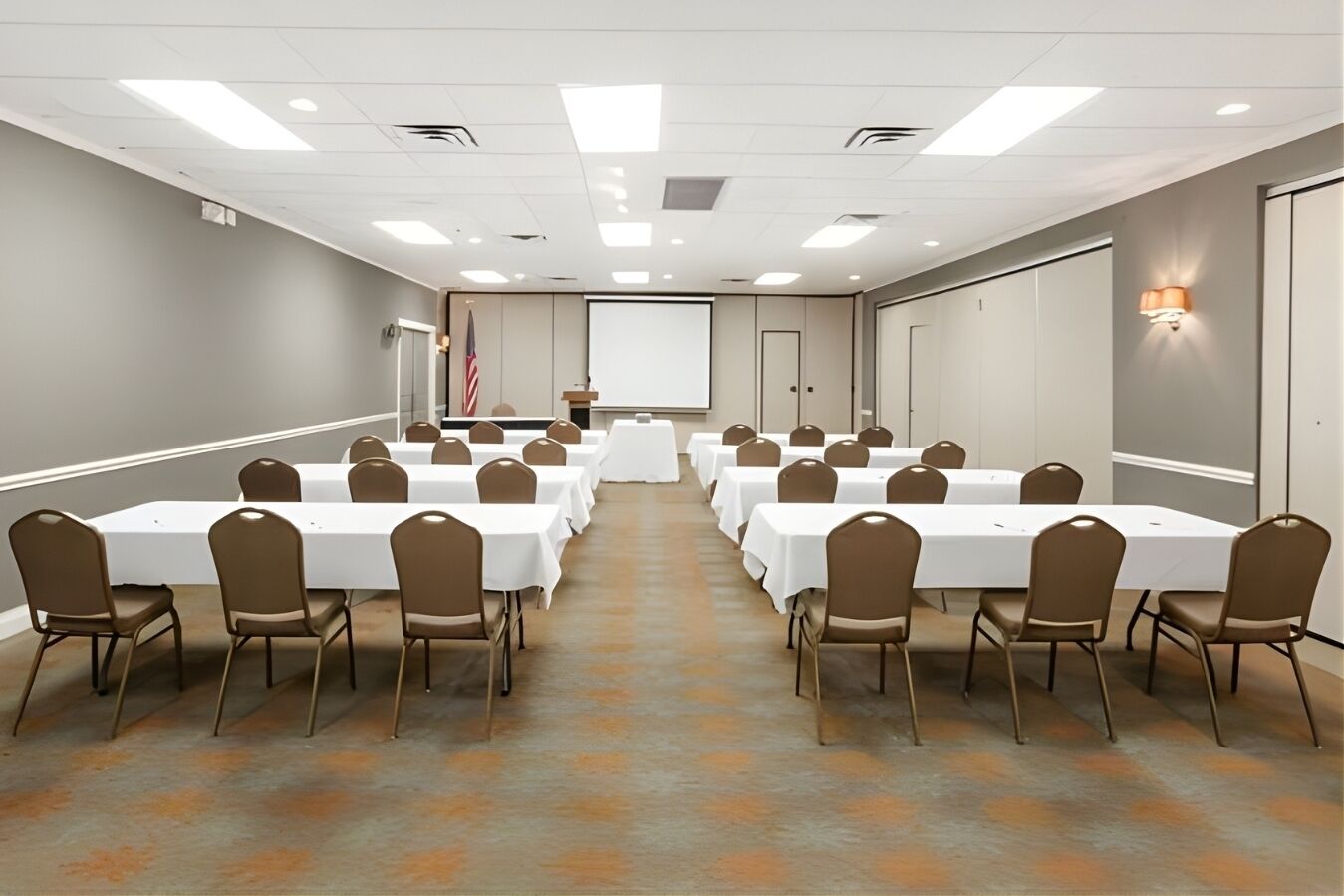 A conference room with multiple tables and chairs, a projector screen, and a podium with an American flag.