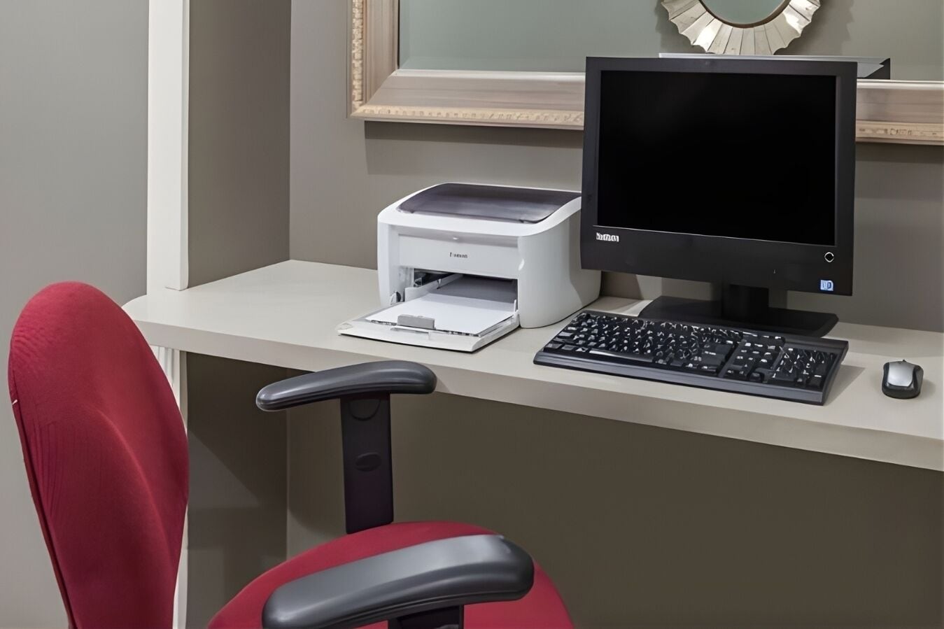 Un espacio de trabajo con un ordenador de escritorio, una impresora y una silla de oficina roja.