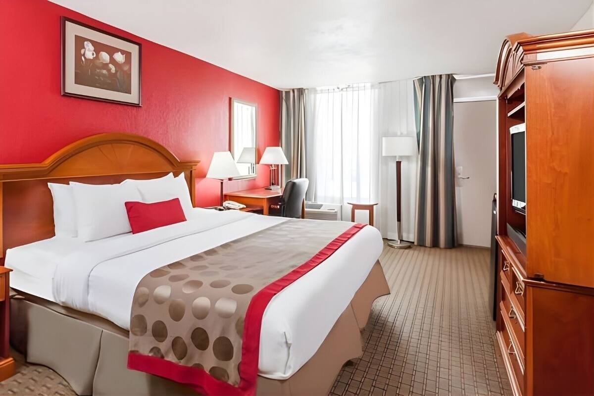 Habitación de hotel con una cama grande, cabecera de madera, escritorio con silla, televisión y armario.