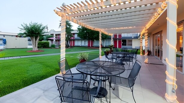 An outdoor patio with tables and chairs, a covered area with string lights, and a well-maintained lawn. - Iberia House & Suites (New Iberia)