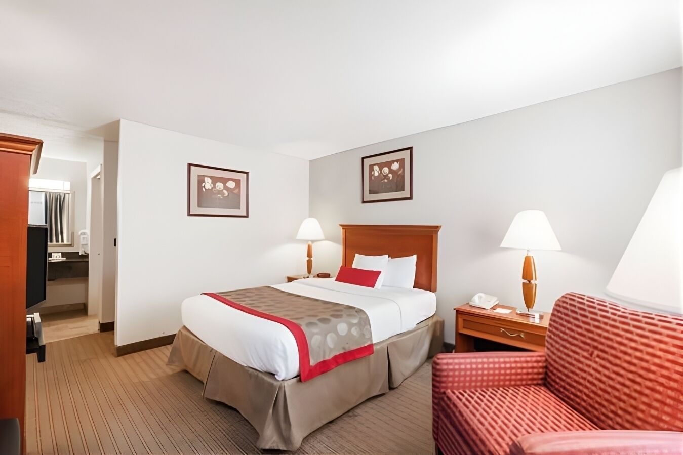 A hotel room with a bed, two bedside tables, a chair, and a door leading to a bathroom.