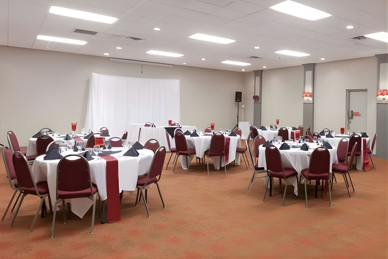 Une salle de conférence dotée de plusieurs tables rondes, chacune étant agrémentée de chaises rouges et de nappes blanches.