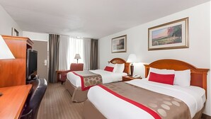 A hotel room with two beds, a desk, a TV, and a window with curtains. - Iberia House & Suites (New Iberia)