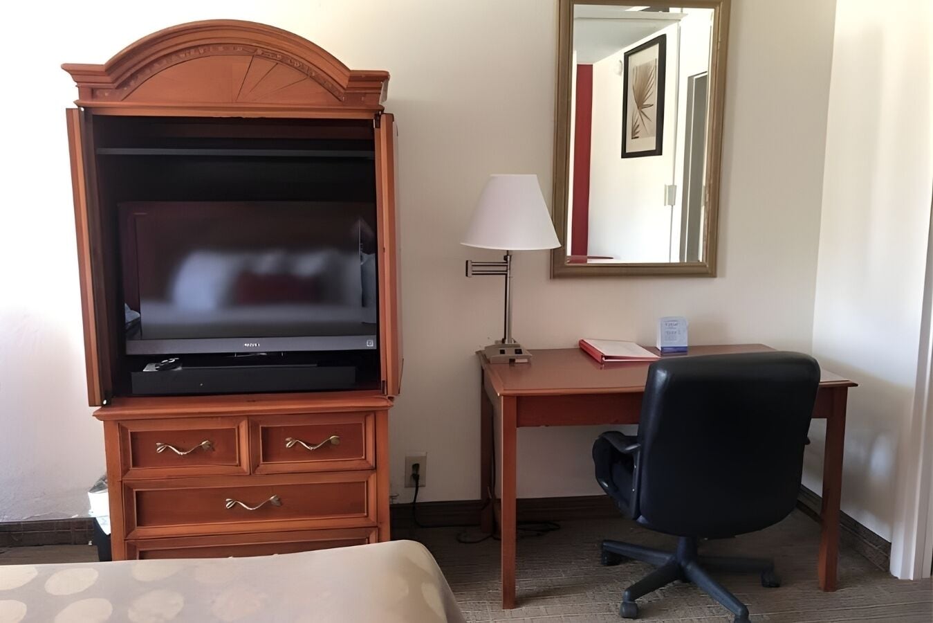 Habitació d'hotel amb escriptori de fusta, cadira d'oficina negra, televisió, làmpada i mirall.