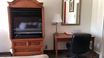 A hotel room with a wooden desk, a black office chair, a television, a lamp, and a mirror.