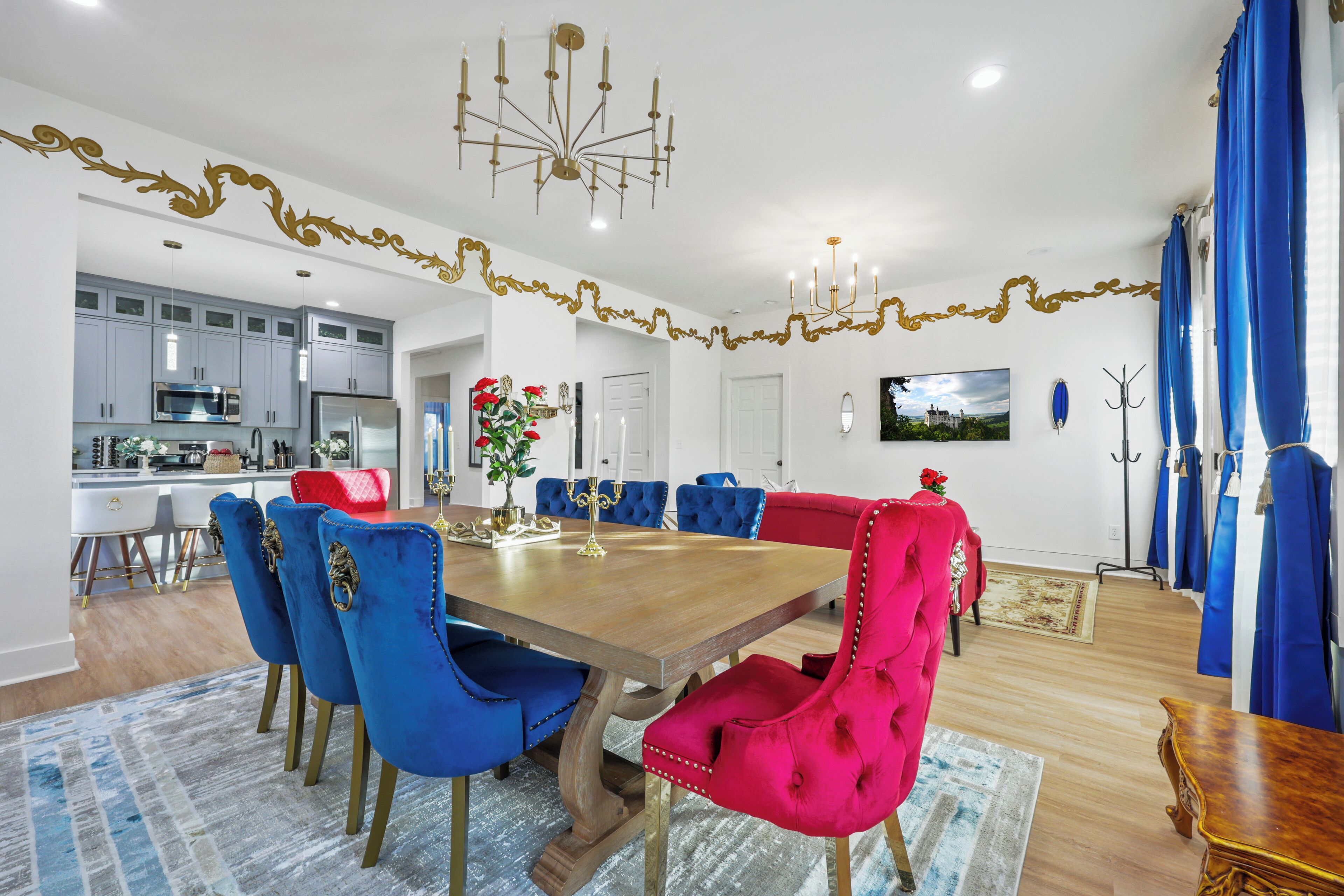 A dining area with a wooden table, blue and red chairs, and a chandelier.