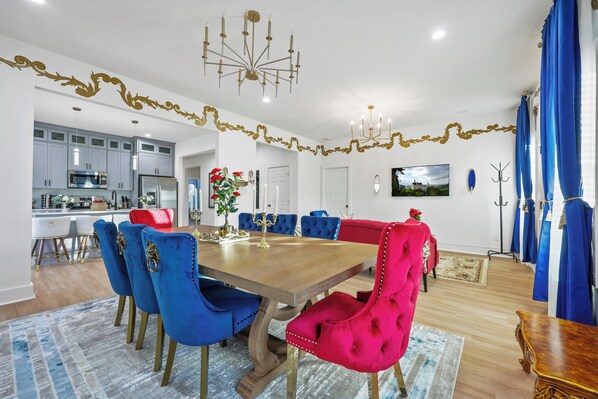 Un coin repas avec une table en bois, des chaises bleues et rouges, et un lustre.