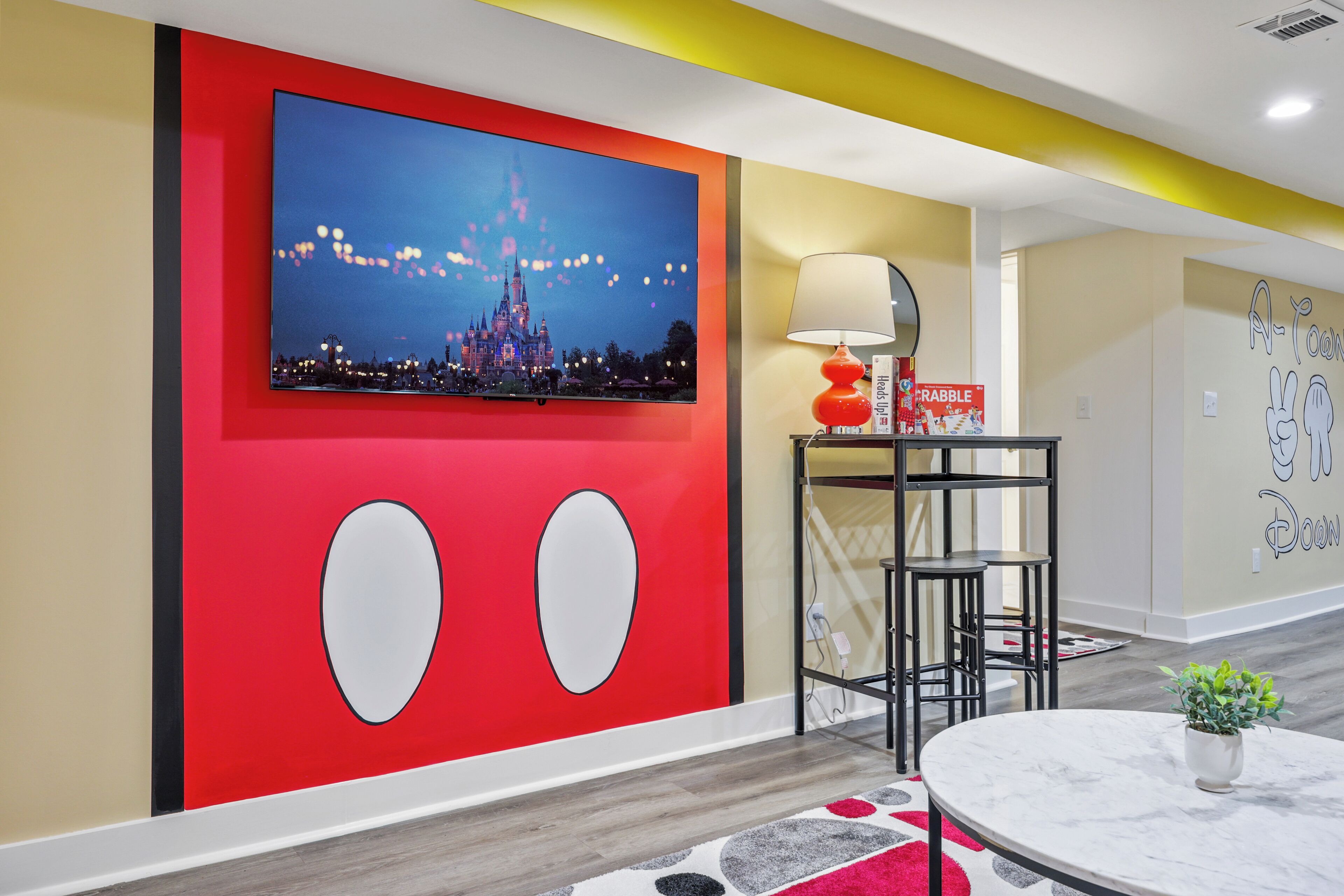 A modern interior with a large flat-screen TV mounted on a red wall, a table with a lamp, and a small potted plant.