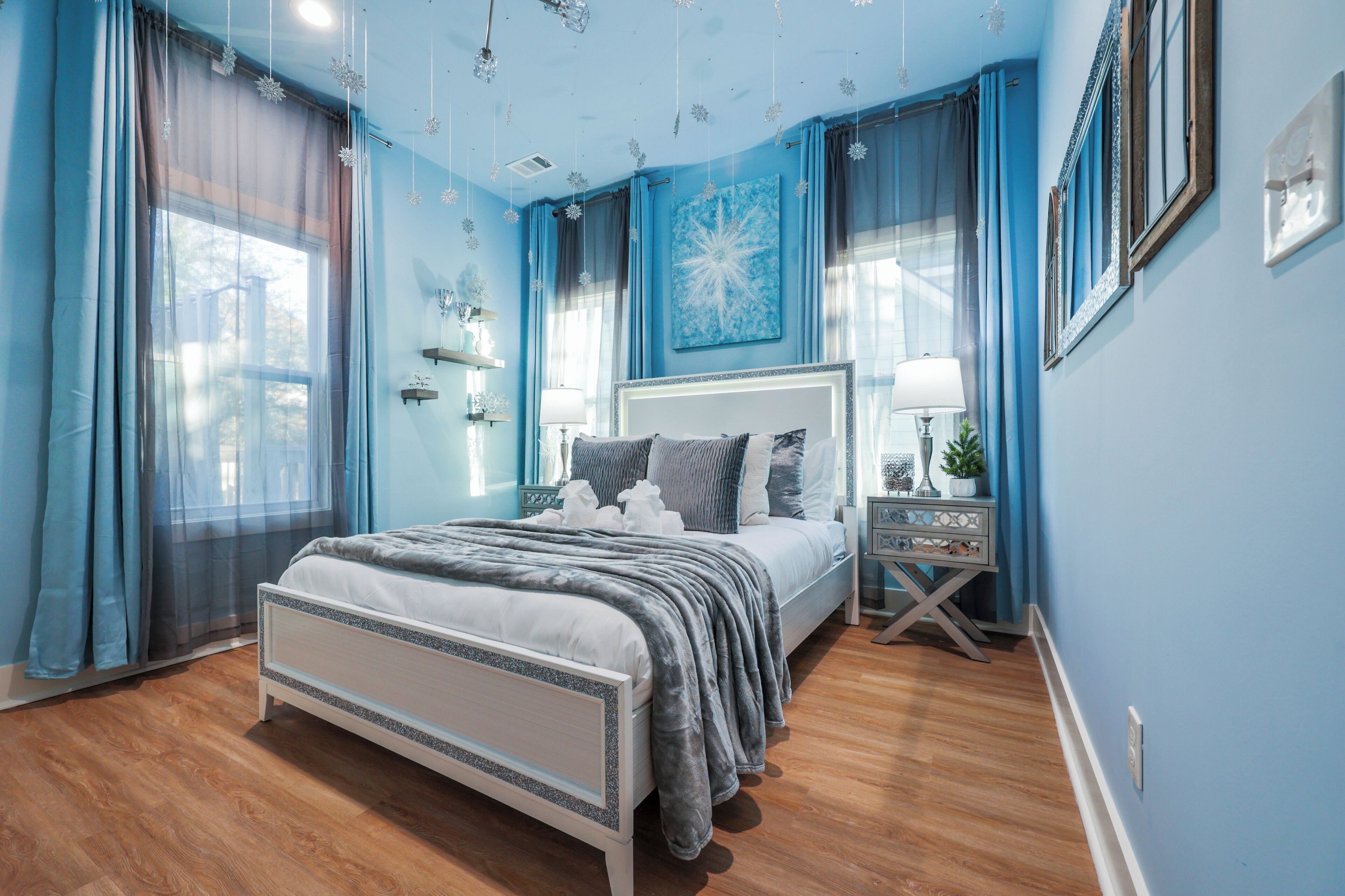 A bedroom with a bed, bedside tables, a nightstand, a window with curtains, and a wall with a picture.