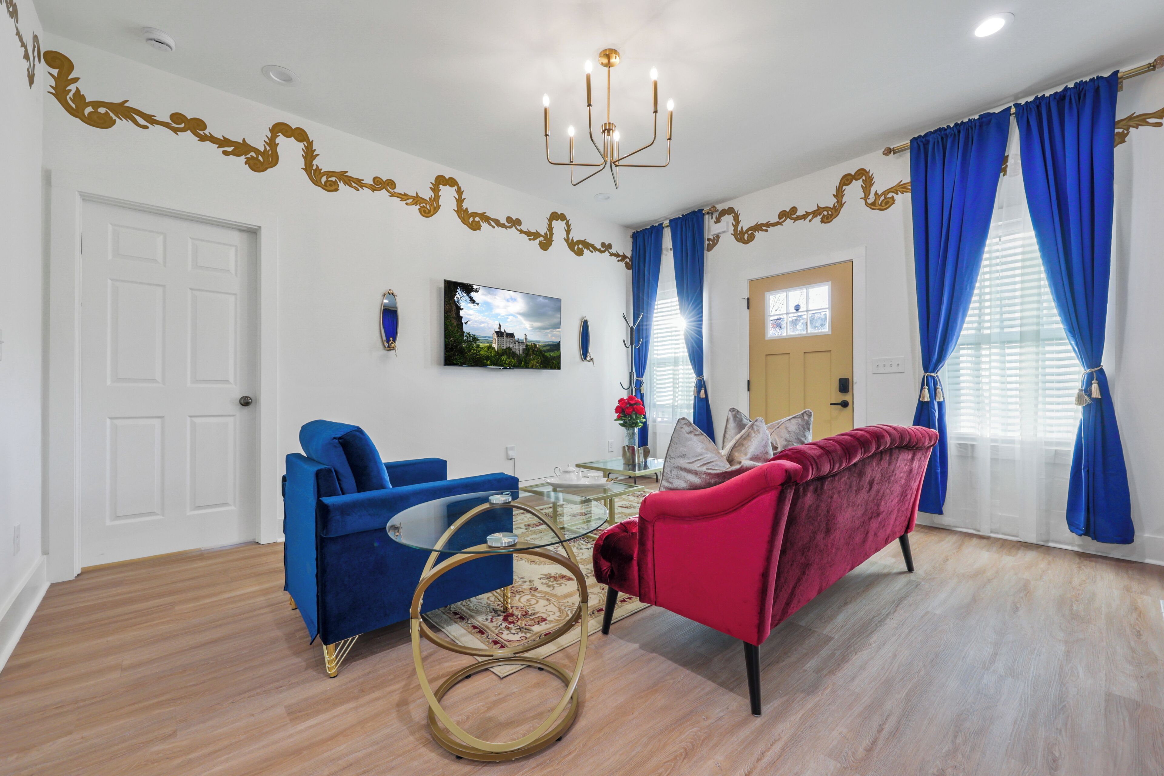 A living room with a blue armchair, a red sofa, a glass coffee table, and a chandelier.