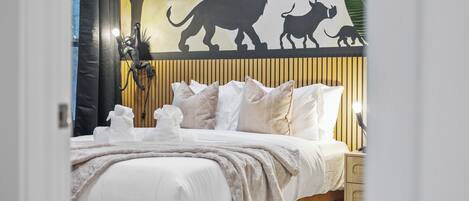 Un dormitorio con cama, almohadas, una mesita de noche y un mural en la pared.