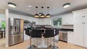 A modern kitchen with white cabinets, stainless steel appliances, and a central island with bar stools. - Riverfront City Escape w/Hot Tub, 2 King, Gym, Sleeps 12, Firepit, Kayaks (Winnipeg)