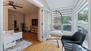 Un salón amplio con un sofá blanco, una silla negra, un sillón colgante y un televisor sobre un mueble de madera.