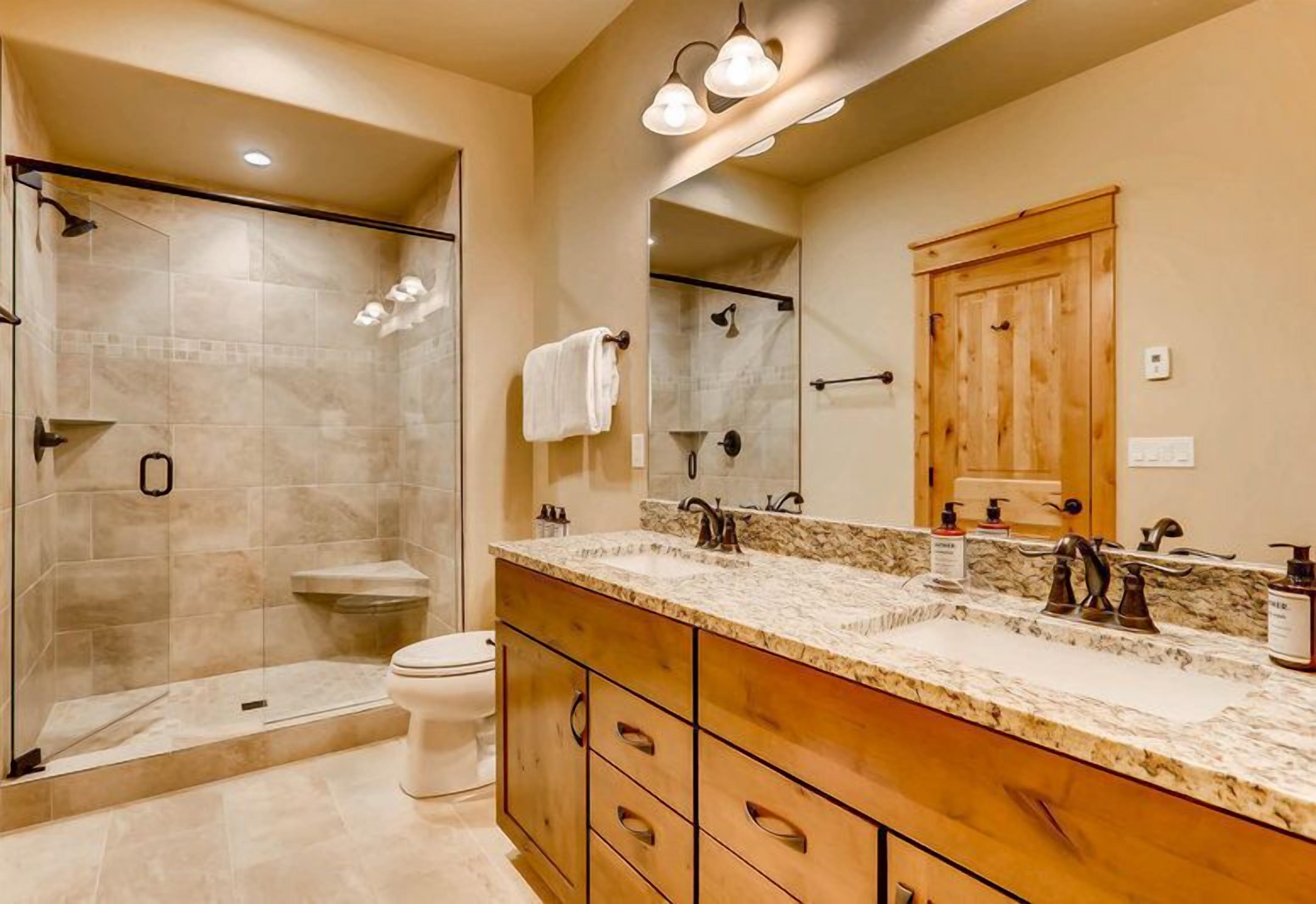 A modern bathroom with a glass-enclosed shower, a vanity with a large mirror, and a toilet.