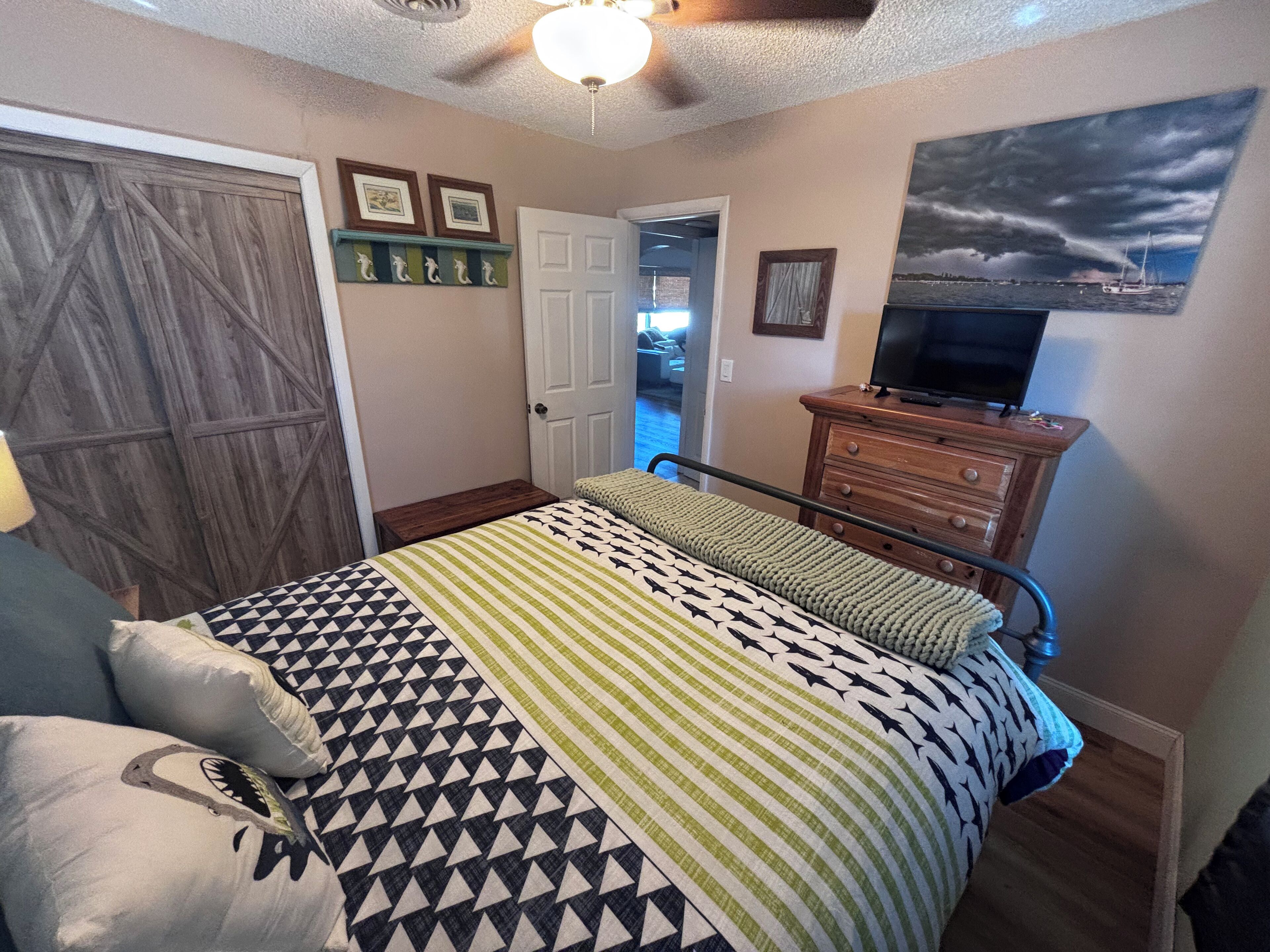 Quarto com uma cama, uma cômoda, uma televisão em cima e uma porta que dá para outro espaço.