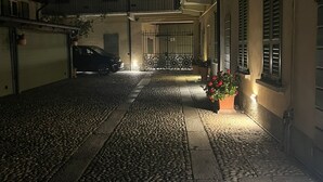 A nighttime street view with cobblestone pavement, a parked car, and a building with a balcony and shutters. - Apartment i13-C Via Pusterla, 8 - Magenta MI - Rho Fiera-Milano-Aeroporto MPX (Magenta)