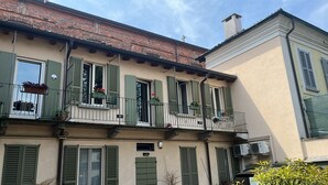 A multi-story building with green shutters, balconies with potted plants, and an air conditioning unit on the exterior wall. - Apartment i13-C Via Pusterla, 8 - Magenta MI - Rho Fiera-Milano-Aeroporto MPX (Magenta)