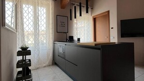 A modern kitchen with a wooden ceiling, a built-in island, pendant lights, and a view of the outside through a window with patterned curtains. - Apartment i13-C Via Pusterla, 8 - Magenta MI - Rho Fiera-Milano-Aeroporto MPX (Magenta)