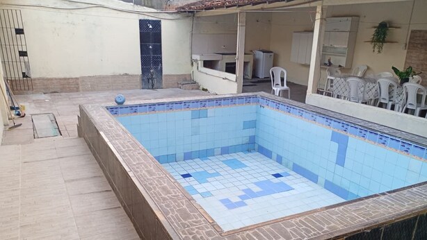 Une piscine rectangulaire aux carreaux bleus et bordée de pierres, entourée d’une terrasse carrelée.