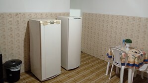 Une petite cuisine avec deux réfrigérateurs blancs, une table recouverte d’une nappe à motifs floraux et une chaise.