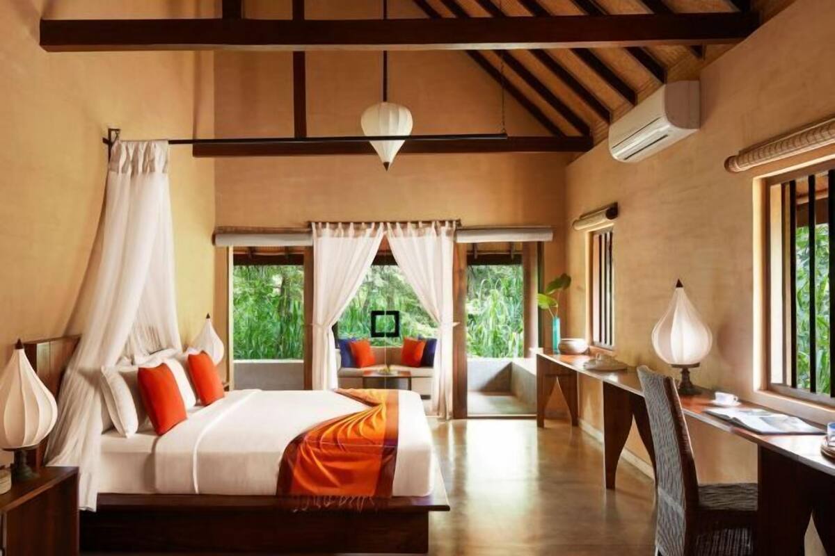 A bedroom with a bed, bedside tables, a desk, a chair, a window, and a view of greenery.
