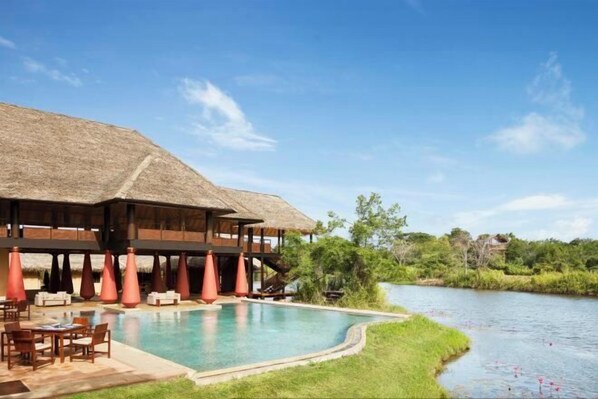 Un área junto a la piscina con una estructura de techo de paja, mobiliario exterior y vistas a un río.