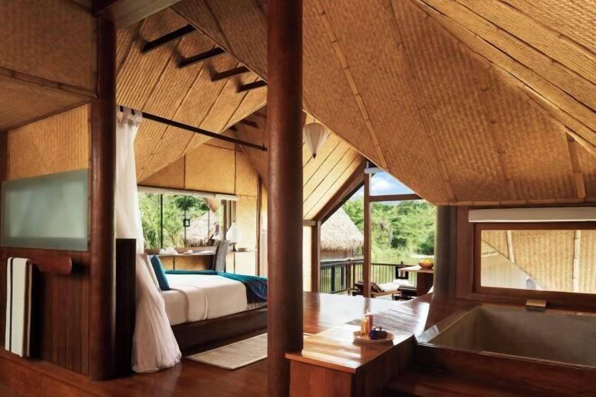 A wooden interior with a bed, a small table, and a window overlooking greenery.