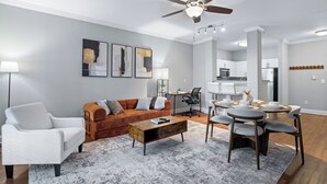 A modern living room with a white sofa, a brown sofa, a coffee table, and a dining area with a round table and chairs. - King Bed Suite | Rooftop Pool | Gym | Private Balcony | Midtown ATL (Atlanta)