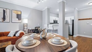 A modern living room with a dining table set for four, a sofa, and a kitchen in the background. - King Bed Suite | Rooftop Pool | Gym | Private Balcony | Midtown ATL (Atlanta)