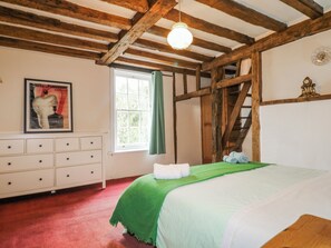Een slaapkamer met een houten plafond, een bed met een groene spreidek, een dressoir, een raam met gordijnen, en een poster aan de muur.