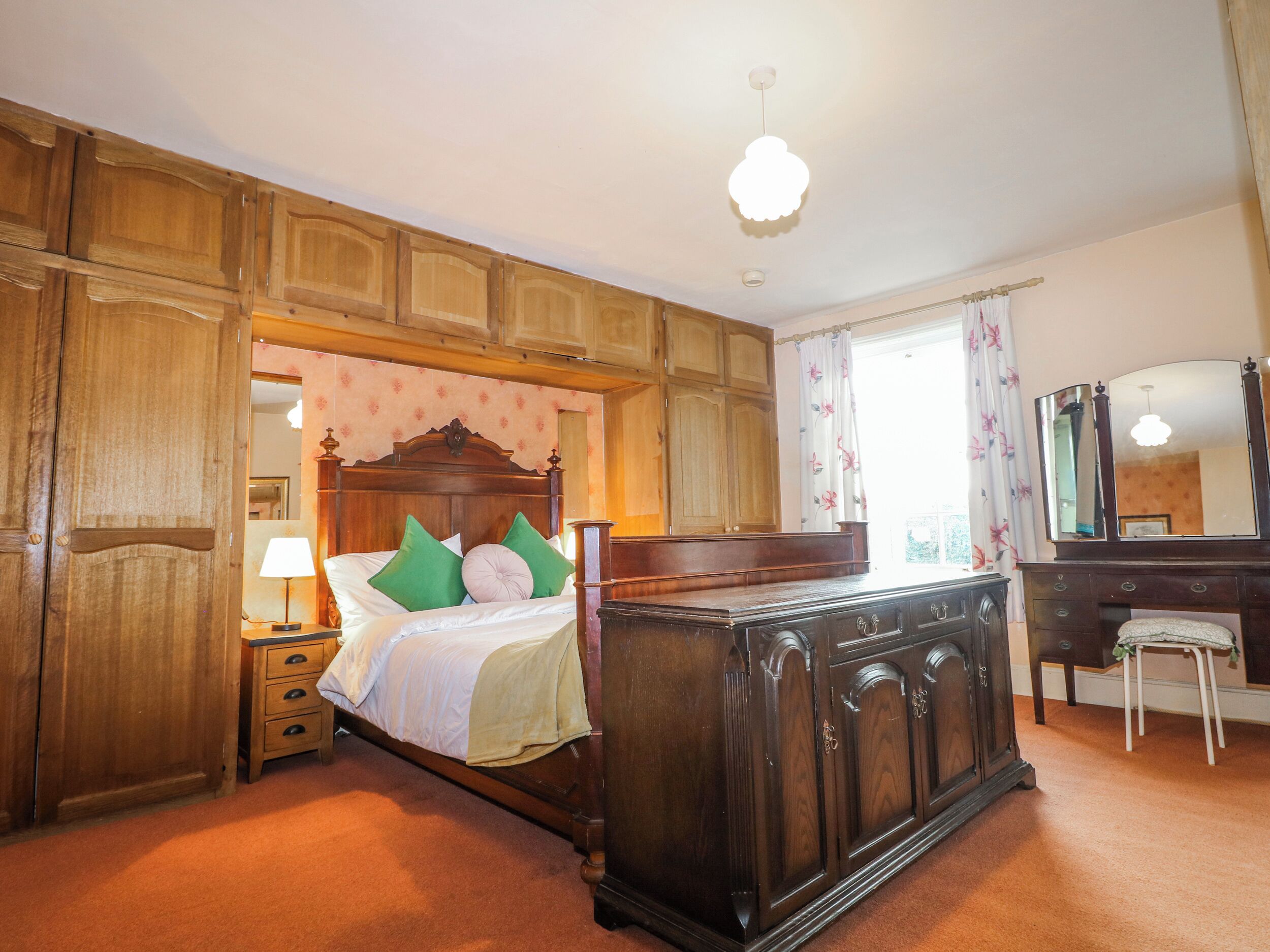 Un dormitorio con cama de madera, mesita de noche, cómoda, espejo y ventana con cortinas.