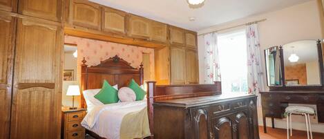 Un dormitorio con cama de madera, mesita de noche, cómoda, espejo y ventana con cortinas.