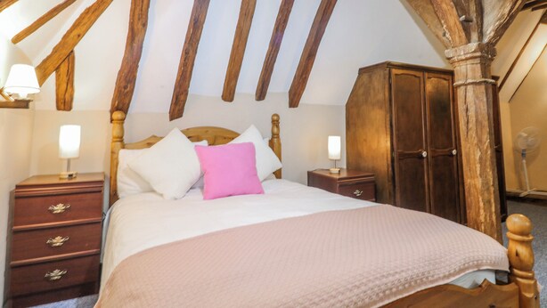 A bedroom with a wooden ceiling, a bed with white and pink bedding, wooden nightstands, and a wardrobe. - Chilton Manor House (Sittingbourne)