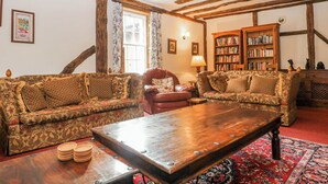 A room with exposed wooden beams, a patterned sofa, a wooden coffee table, a red armchair, a bookshelf, and a patterned rug. - Chilton Manor House (Sittingbourne)