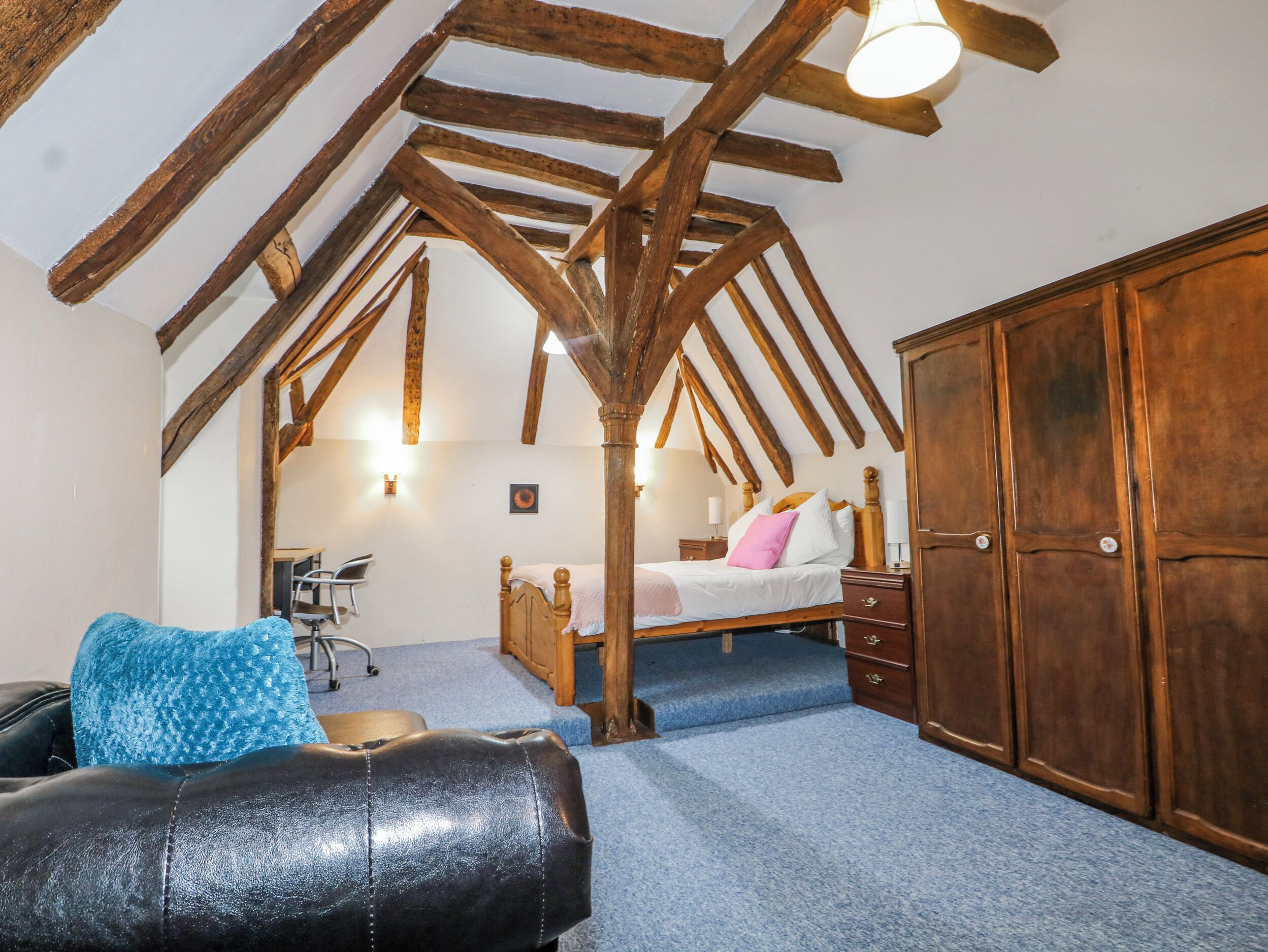 A bedroom with a loft-style ceiling, a bed, a wardrobe, and a desk with a chair.