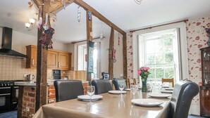 A dining area with a table set for four, a brick wall, wooden beams, and a window with a view. - Chilton Manor House (Sittingbourne)
