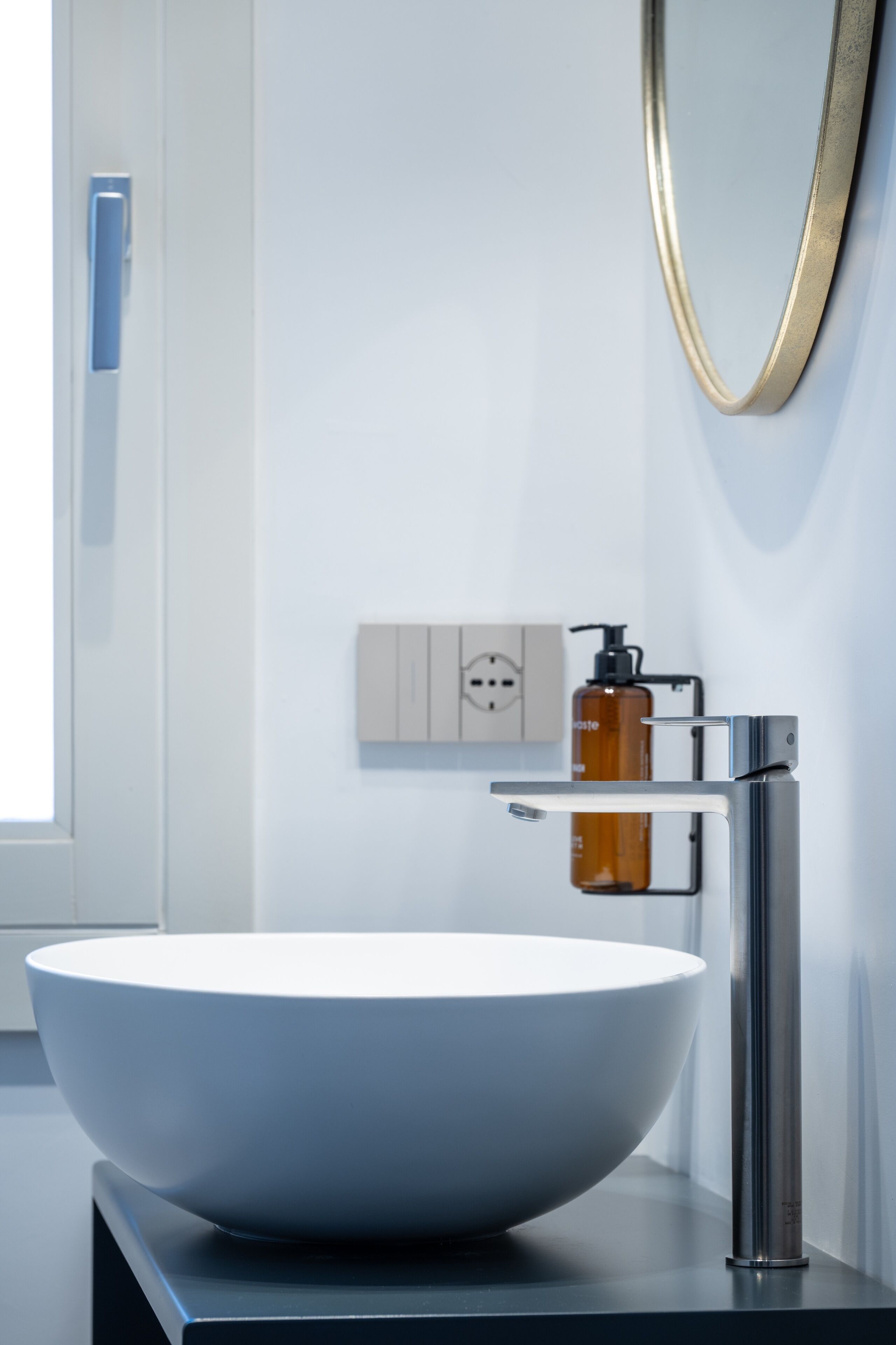 A modern bathroom with a large white vessel sink, a chrome faucet, and a wall-mounted mirror.