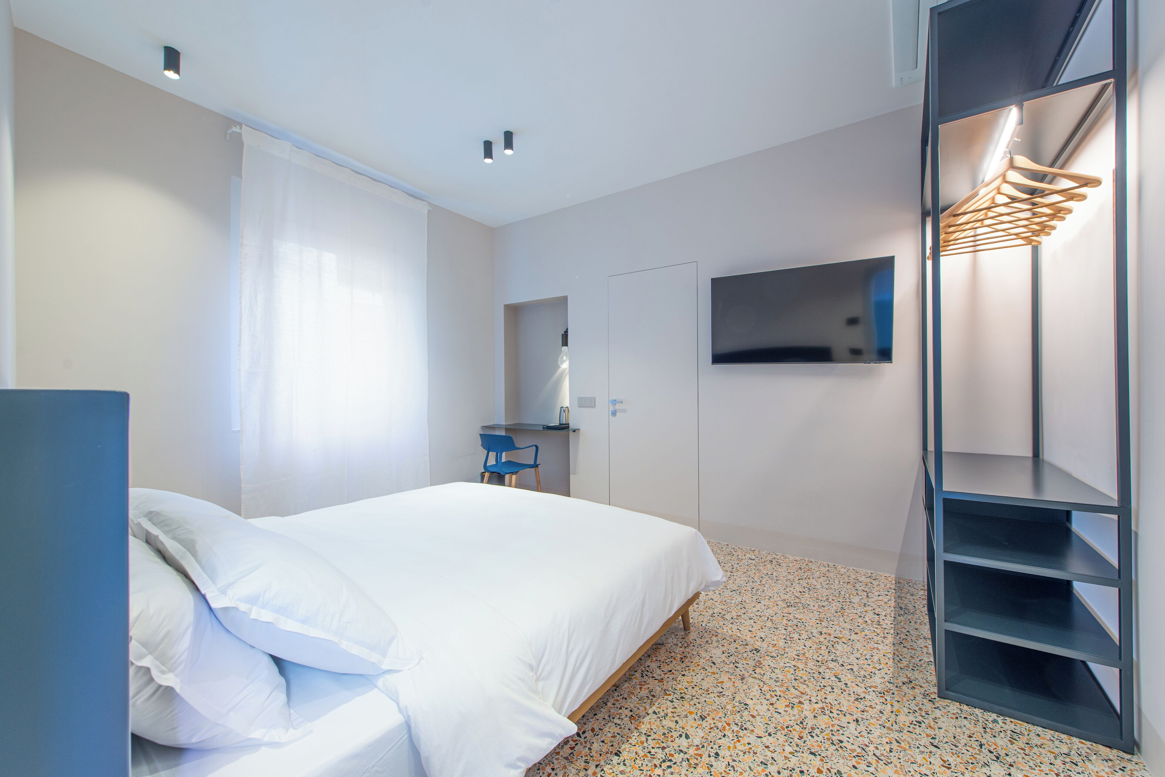 Una habitación de hotel moderna con una cama, un escritorio, una silla, un televisor y un armario.