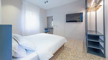 Una habitación de hotel moderna con una cama, un escritorio, una silla, un televisor y un armario.