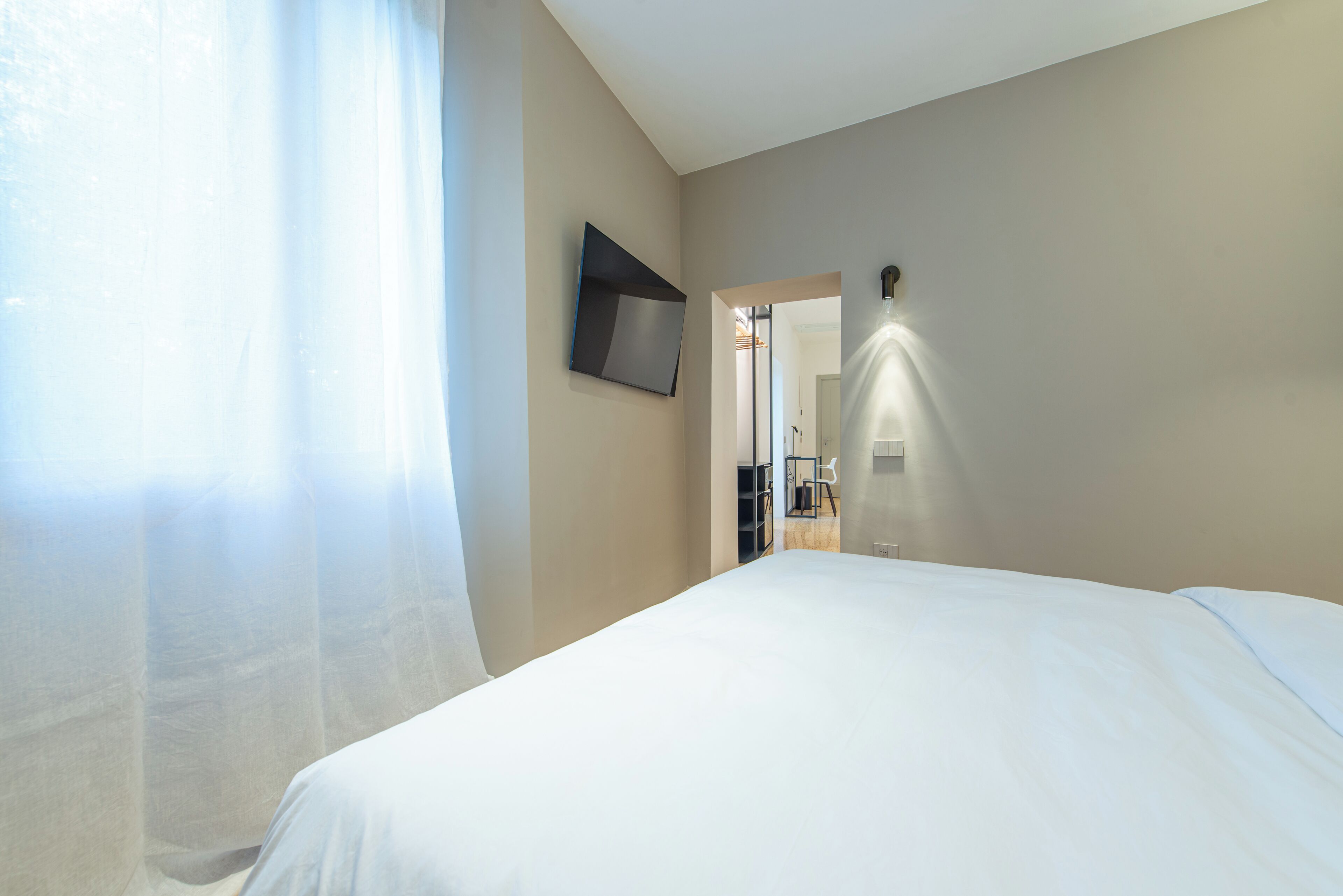 A hotel room with a large bed, a flat-screen TV mounted on the wall, and a doorway leading to a bathroom.