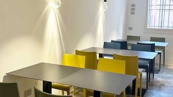 Uma sala de conferência moderna com uma mesa comprida, cadeiras amarelas e verdes, e luminárias pendentes.