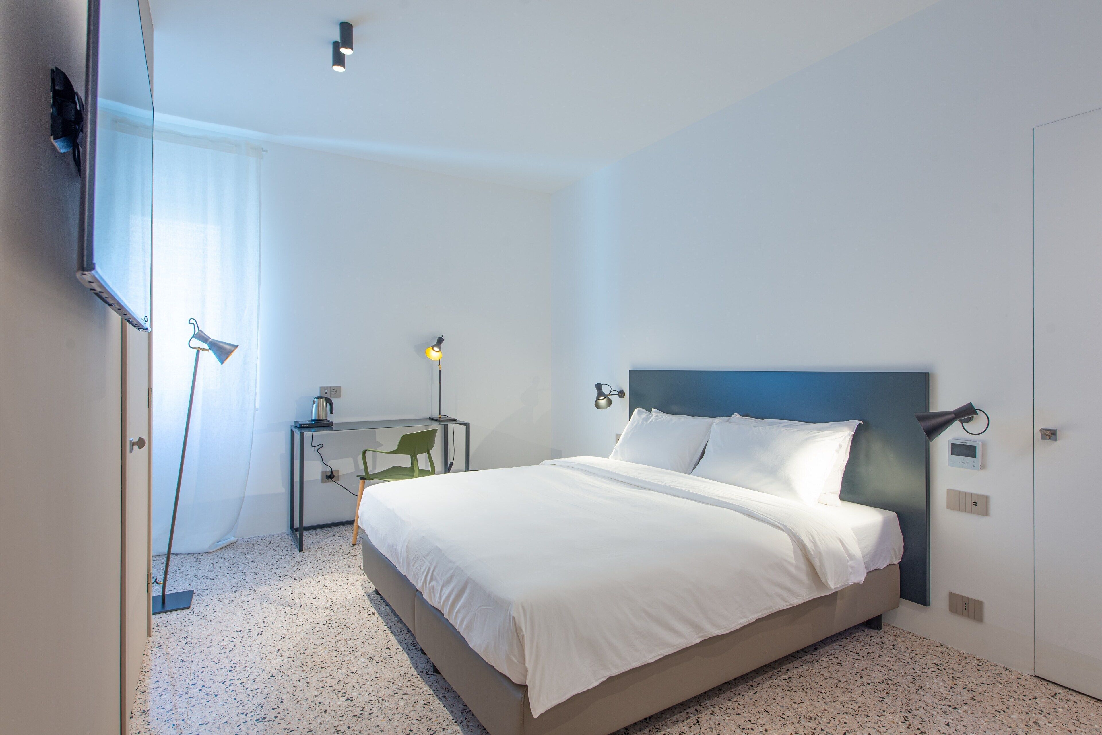 A modern hotel room with a large bed, a desk, and a TV mounted on the wall.