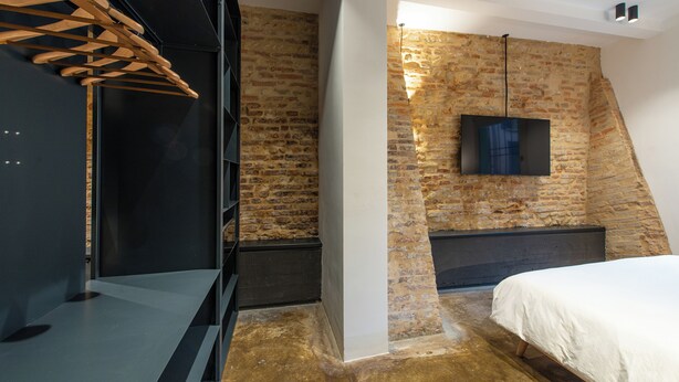 A bedroom with a sloped ceiling, exposed brick walls, a flat-screen TV mounted on the wall, and a bed with a white bedspread. - Ca Moro - Rooms and Apartments (Rimini)