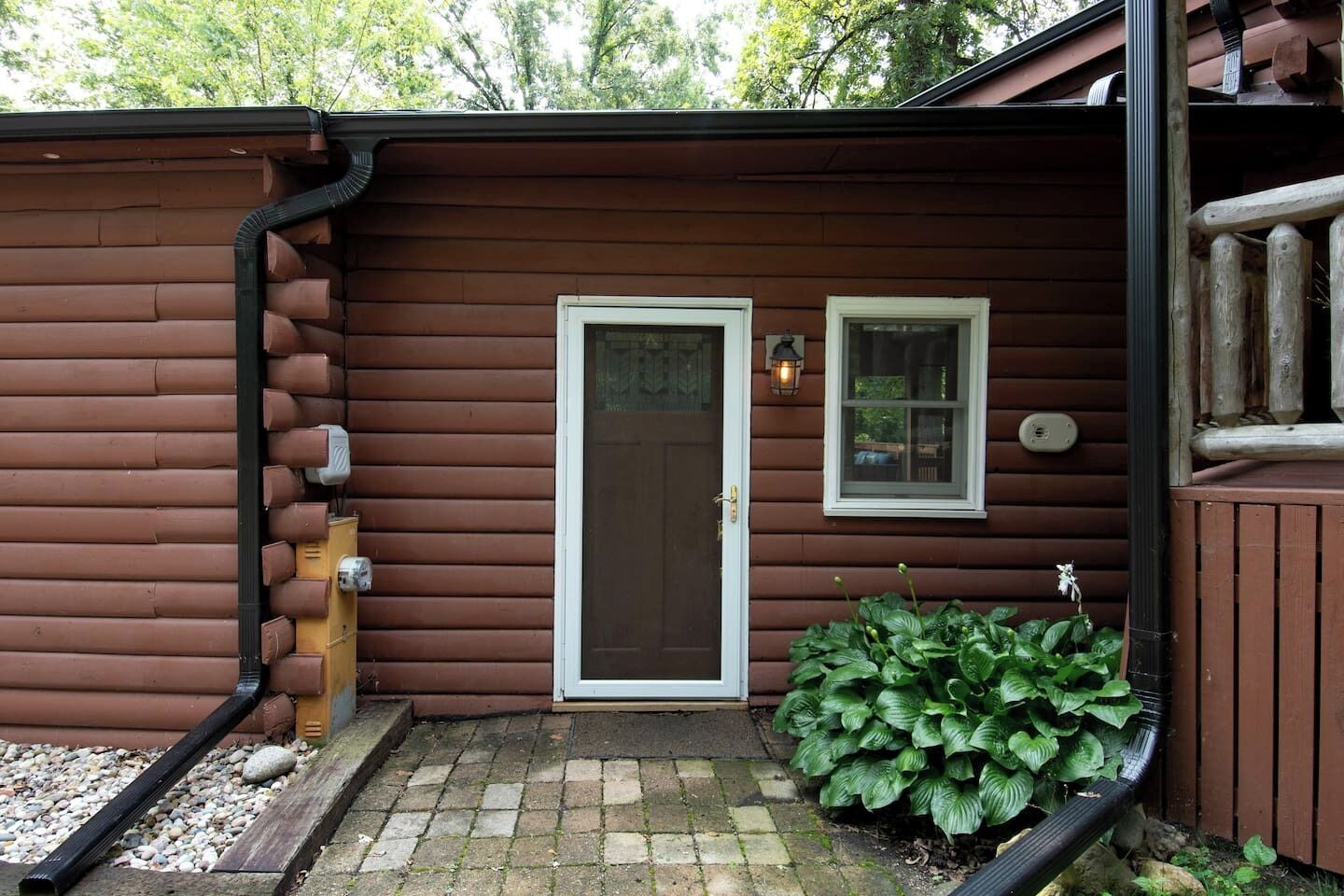 Une cabane en bois avec une porte d’entrée, une petite fenêtre et un pot de fleurs.