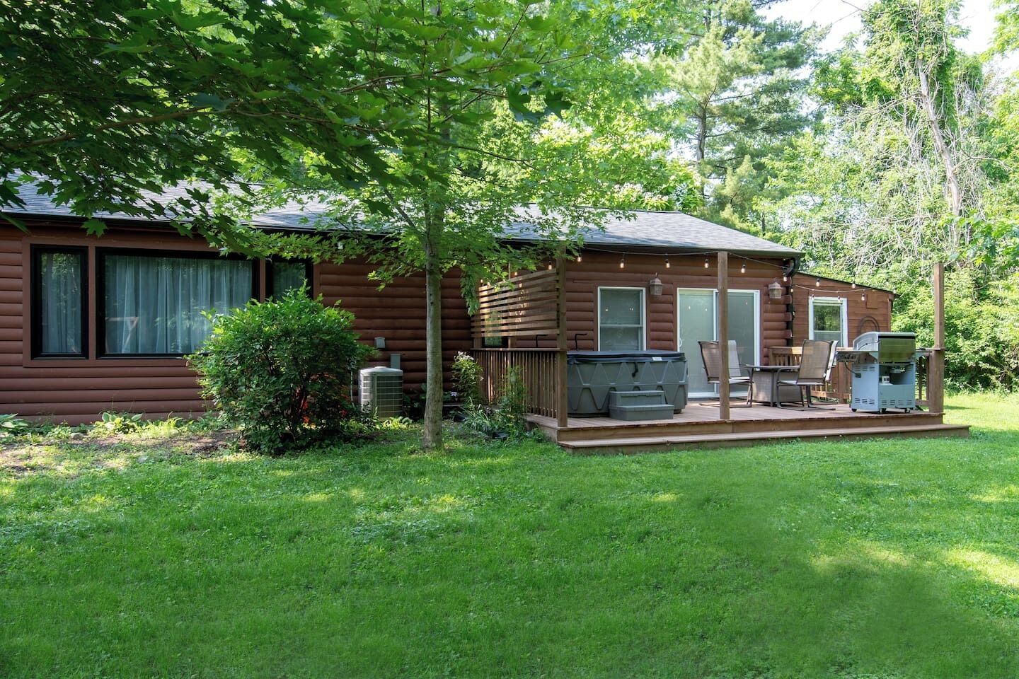 A log cabin with a deck, outdoor seating, and a grill.