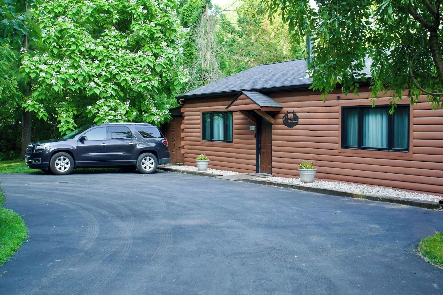 A log cabin with a car parked in front, surrounded by lush greenery.