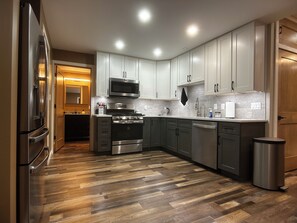 Una cocina moderna con electrodomésticos de acero inoxidable, piso de madera y armarios de colores claros.