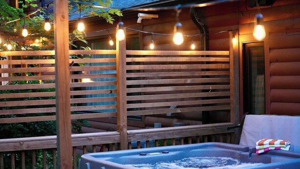 Una terraza de madera con un jacuzzi, luces colgantes y una valla de madera.